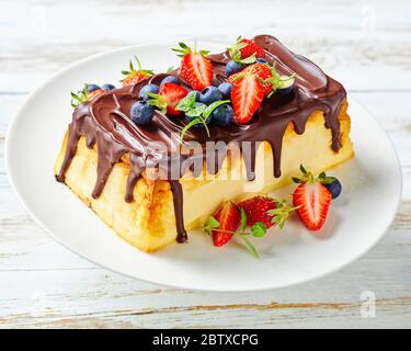 Lviv syrnyk von Quark Käse, Butter, Rosinen mit Schokolade gekrönt serviert mit frischen Beeren Heidelbeeren, Erdbeeren, Minze auf einem weißen Holzrückerfisch Stockfoto