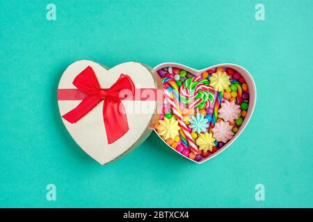 Mix bunte Schokolade Süßigkeiten liegen in Geschenkbox Form von Herz auf bunten Hintergrund Flat Lay Top-Ansicht Stockfoto