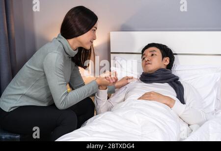 Frau besucht und kümmert sich um ihren kranken Mann, während er zu Hause auf einem Bett liegt Stockfoto