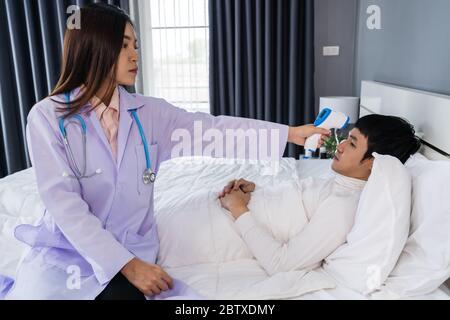 Arzt mit Infrarot-Stirnthermometer (Thermometer Pistole) zur Messung der Temperatur des kranken Mannes im Bett Stockfoto