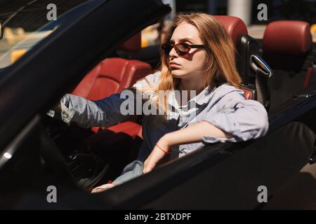 Junge ernsthafte Dame in Sonnenbrille nachdenklich Fahren Cabrio Auto Stockfoto