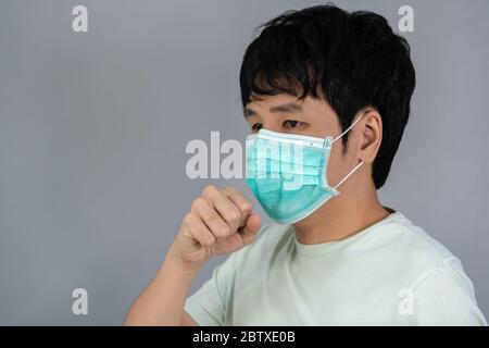Kranker junger Mann, der eine chirurgische Maske (medizinische Maske) trägt, hustet Stockfoto