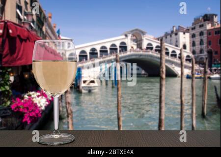 Glas Weißwein mit Blick auf den berühmten Canal Grande und die Rialtobrücke in Venedig, Italien Stockfoto