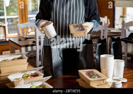 Restaurantmitarbeiter tragen Schutzmaske und Handschuhe Verpackung Lebensmittel verpackt mitnehmen. Lebensmittelzustellung und kontaktloser Online-Lebensmitteleinkauf. Stockfoto