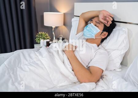 Kranker Mann in medizinischer Maske ist Kopfschmerzen und Leiden an Viruserkrankung und Fieber im Bett, Coronavirus (Covid-19) Pandemie Konzept. Stockfoto