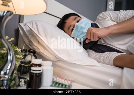 Kranker Mann in medizinischer Maske hustet und leidet an Viruserkrankung und Fieber in einem Bett, Coronavirus (Covid-19) Pandemie Konzept. Stockfoto