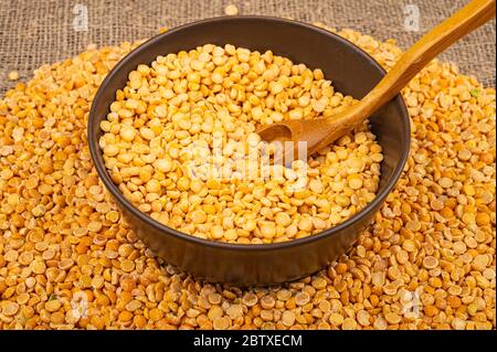 Gelbe Erbsen in einer Keramikschale und grits auf einem Hintergrund von grob strukturierten Burlap verstreut. Traditionelles Getreide für die Herstellung von Suppen und Porridge. Stockfoto