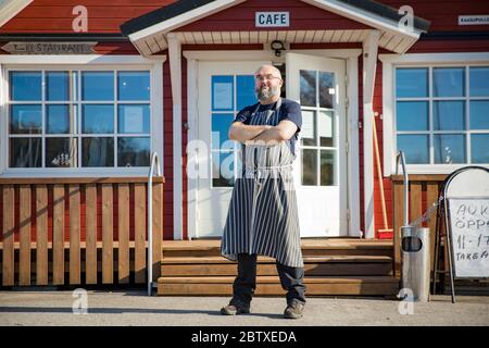 Porträt eines selbstbewussten reifen Mannes mit Bart, Restaurantangestellter mit Schürzen vor dem Restaurant. Konzept für kleine Unternehmen. Stockfoto