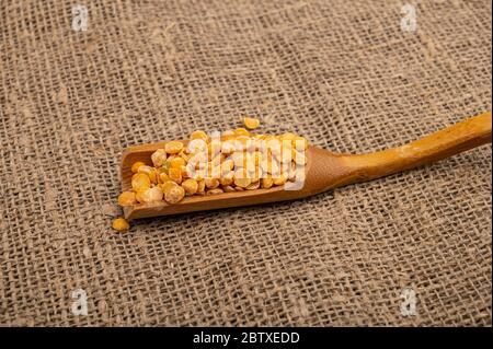 Gelbe Erbsen in einem Holzlöffel auf einem Hintergrund von Burlap mit einer rauen Textur gespalten. Traditionelles Getreide für die Herstellung von Suppen und Porridge. Nahaufnahme Stockfoto