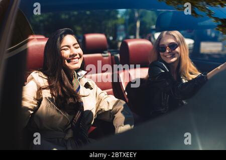 Zwei fröhliche Mädchen verbringen gerne Zeit zusammen mit dem Cabriolet auf den Straßen der Stadt Stockfoto