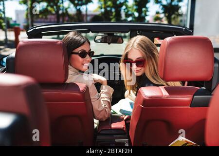 Schöne Mädchen in Sonnenbrille glücklich suchen in der Kamera verbringen Zeit zusammen, während der Fahrt Cabrio Auto auf Straßen der Stadt draußen Stockfoto