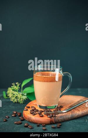 Dalgona Kaffee mit Schaum in Glasbecher auf Schneidebrett, Kaffeebohnen und Metallstroh, schwarzer Hintergrund, Nahaufnahme Stockfoto