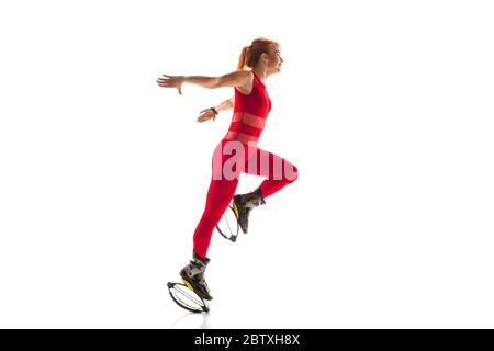 Schöne Rotschopf Frau in einer roten Sportbekleidung Springen in einem kangoo springt Schuhe isoliert auf weißem Studio-Hintergrund. Hoch springen, aktive Bewegung, Action, Fitness und Wellness. Modell mit Innengewinde montieren. Stockfoto