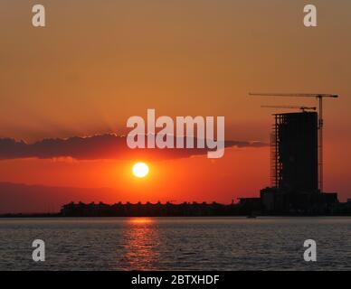 Bau- und Ski-Scraper-Gebäude und Kran gegen bunten Himmel mit Sonne. Baukonzept. Stockfoto