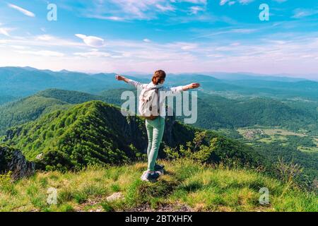 Mädchen Tourist mit Rucksack steht am Rande einer Klippe mit ausgestreckten Armen. Wandern, Tourismus, Freiheitskonzept. Stockfoto