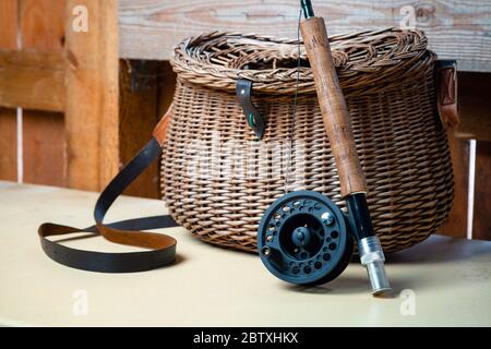 Nahaufnahme der Fliegenfischerei mit Rolle neben geflochtenem Korb. Fliegenfischen Ausrüstung Stillleben. Niemand Stockfoto