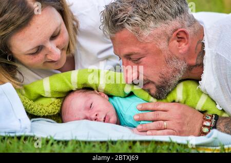 Neugeborenes Baby liegt draußen im Stadtpark mit seinen Eltern, die sich um ihn kümmern. Stockfoto