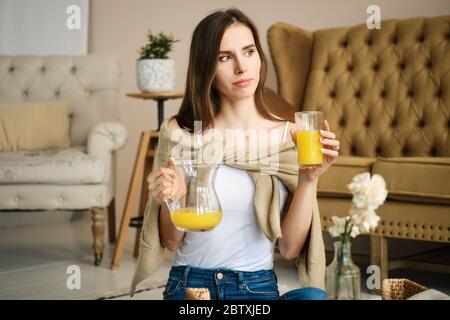 Lächelndes Mädchen mit Klammern hält Glas und Krug mit Saft in den Händen Stockfoto