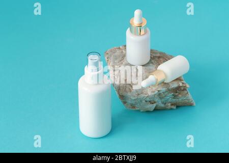 Kosmetisches Tonikum, Feuchtigkeitscreme und Serum in weißen Tropfflaschen auf Naturstein. Blauer Hintergrund, natürliche Hautpflege-Produkte Konzept. Stockfoto