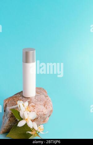 Kosmetische Serum-Flasche in weiß blank Paket auf dem Stein mit Jasminblüte, blauer Hintergrund, Kopierer Raum. Selektiver Fokus Stockfoto