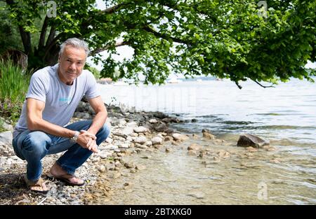 Utting, Deutschland. Mai 2020. EXKLUSIV - Hannes Jaenicke, Schauspieler, sitzt während einer Fotosession am Ammersee. Für eine ZDF-Dokumentation hat sich der Schauspieler mit dem Fisch beschäftigt. Der Film "Hannes Jaenicke: In Aktion für den Lachs" wird am 16. Juni um 22.15 Uhr im ZDF ausgestrahlt. Kredit: Sven Hoppe/dpa/Alamy Live News Stockfoto