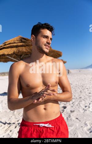 Kaukasischer Mann genießt Zeit am Strand an einem sonnigen Tag, stehen und mit blauen Himmel im Hintergrund wegschauen Stockfoto