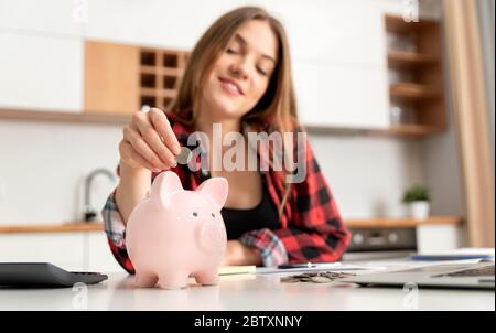 Frau, die Geld in Sparschwein am Tisch legt. Haushaltskonzept für zu Hause Stockfoto