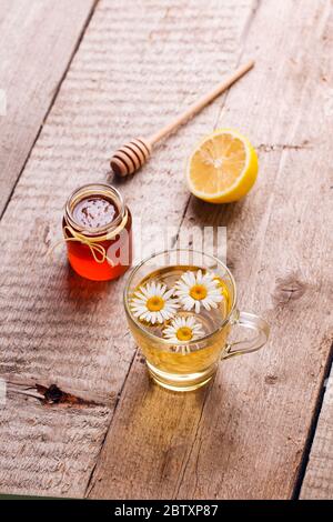 Gesunder Kamille Tee in Glasbecher gegossen. Teekanne, kleines Honigglas, Heidekraut und Glas mit Gänseblümchen Heilkräutern. Stockfoto