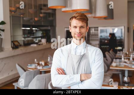 Schöner männlicher Kellner in Schürze, der im Restaurant steht Stockfoto