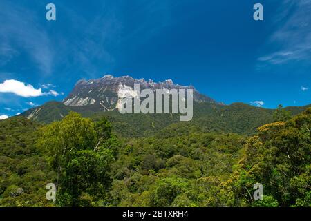 Gipfel und Gipfel des Mount Kinabalu in Sonnenlicht, mit wunderschönen Regenwald im Vordergrund, und Himmel über. Mount Kinabalu, Sabah, Borneo, Malaysia Stockfoto