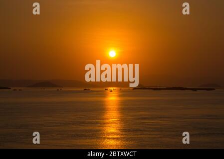 Ein atemberaubender Sonnenuntergang über dem Meer im Komodo Nationalpark, Indonesien, mit Inseln und Booten im fernen Hintergrund. Stockfoto