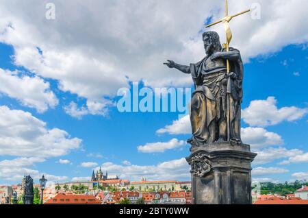 Johannes der Täufer Statue auf der Karlsbrücke Karluv Most über der Moldau mit Prager Burg, St. Veits Kathedrale in Hradcany Bezirk, blauer Himmel weiße Wolken Hintergrund, Böhmen, Tschechische Republik Stockfoto