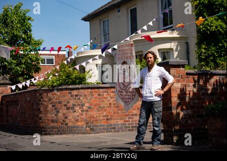 Der Künstler Luke Perry in der Duncombe Street in Wollaston, wo er mit Botschaften der Unterstützung für Nachbarn und Schlüsselarbeiter aufgehängt hat, um einen 500 Meter langen Farbkorridor durch das Dorf West Midlands zu schaffen. Herr Perry bat die Anwohner und Ladenbesitzer, Entwürfe und Botschaften einzureichen, die er dann mit Hilfe von Freiwilligen handbemalt und auf die Amme genäht hatte. Stockfoto