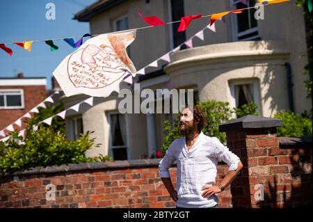 Der Künstler Luke Perry in der Duncombe Street in Wollaston, wo er mit Botschaften der Unterstützung für Nachbarn und Schlüsselarbeiter aufgehängt hat, um einen 500 Meter langen Farbkorridor durch das Dorf West Midlands zu schaffen. Herr Perry bat die Anwohner und Ladenbesitzer, Entwürfe und Botschaften einzureichen, die er dann mit Hilfe von Freiwilligen handbemalt und auf die Amme genäht hatte. Stockfoto