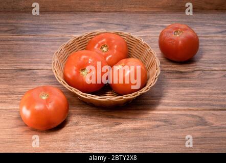 Viele frische rote Tomaten in einem gewebten Korb Holz Hintergrund Nahaufnahme Stockfoto