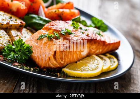 Gebratenes Lachssteak mit Kartoffelchips und Gemüse auf Holztisch Stockfoto