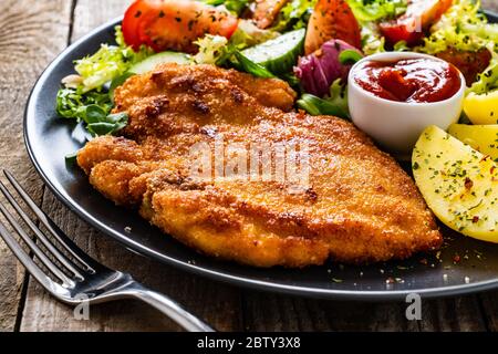 Schnitzel mit gekochten Kartoffeln und Gemüsesalat auf Holzgrund Stockfoto