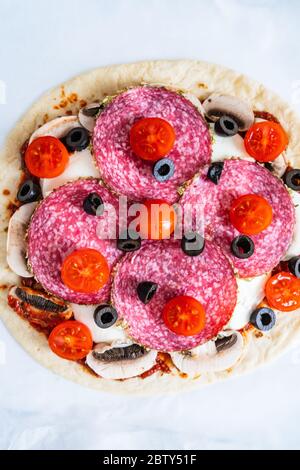 Ungebackene Pizza mit Salami, Champignon, Oliven und Kirschtomaten Stockfoto