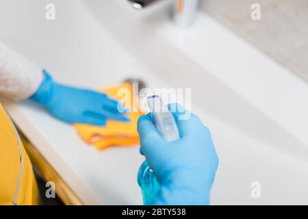 Weibliche Hände tragen Gummihandschuhe halten Mikrofasertuch und Sprühflasche Desinfektionsmittel Waschbecken im Badezimmer zu desinfizieren. Schutz vor Viren oder Bacter Stockfoto