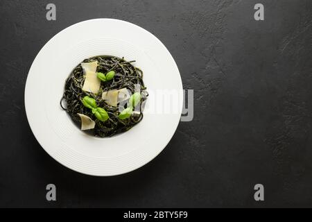 Schwarze Pasta Spaghetti Tintenfisch Tinte mit Sauce Pesto, Basilikum, Käse in Schüssel auf schwarzem Hintergrund. Draufsicht. Kopierbereich. Stockfoto