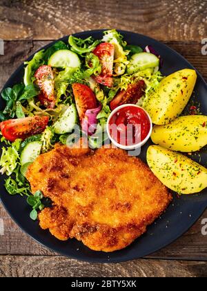 Schnitzel mit gekochten Kartoffeln und Gemüsesalat auf Holzgrund Stockfoto