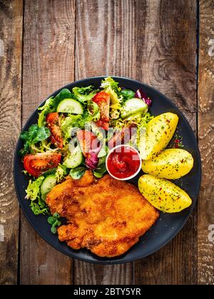 Schnitzel mit gekochten Kartoffeln und Gemüsesalat auf Holzgrund Stockfoto