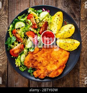 Schnitzel mit gekochten Kartoffeln und Gemüsesalat auf Holzgrund Stockfoto