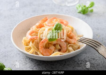 Italienische Pasta Fettuccine mit Garnelen in weißer Schüssel auf grauem Tisch. Nahaufnahme. Stockfoto