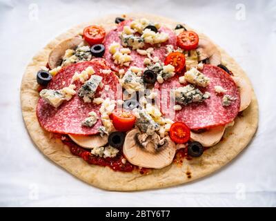 Ungebackene Pizza mit Salami, Champignon, Oliven und Kirschtomaten Stockfoto