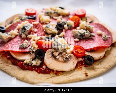 Ungebackene Pizza mit Salami, Champignon, Oliven und Kirschtomaten Stockfoto