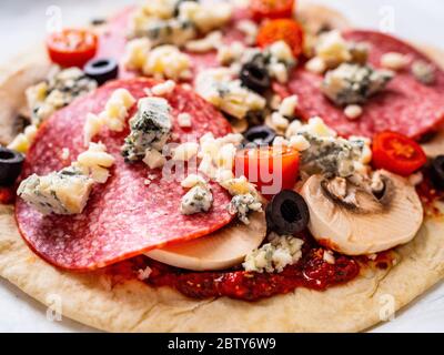 Ungebackene Pizza mit Salami, Champignon, Oliven und Kirschtomaten Stockfoto