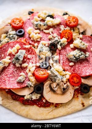 Ungebackene Pizza mit Salami, Champignon, Oliven und Kirschtomaten Stockfoto