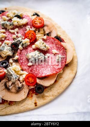 Ungebackene Pizza mit Salami, Champignon, Oliven und Kirschtomaten Stockfoto