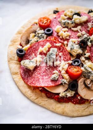 Ungebackene Pizza mit Salami, Champignon, Oliven und Kirschtomaten Stockfoto